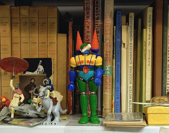 A colourful toy robot standing on a shelf with other pop-culture knick knacks and books in a still from 'Pianeta Rota' (2021)