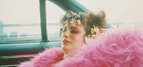 Nan Goldin wearing a pink feather boa in All the Beauty and the Bloodshed