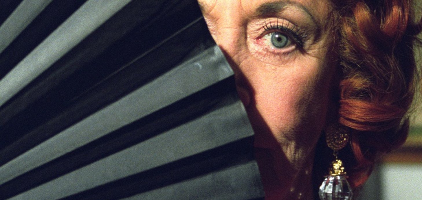 Judi Farr in a still from Unfolding Florence: The Many Lives of Florence Broadhurst (2006), one eye peeking out behind a fan