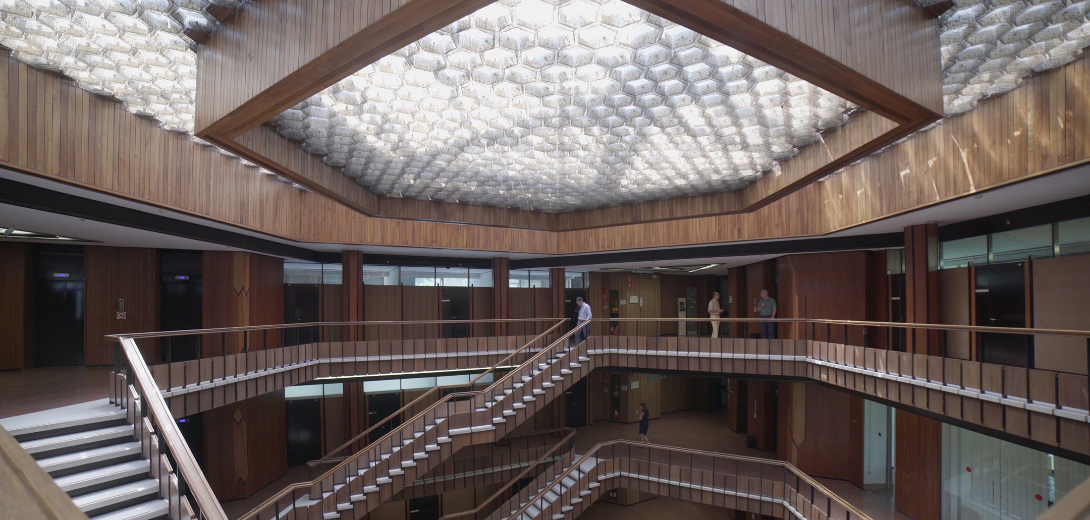 A wide shot of a architecturally designed foyer with wood panels and stairs in a still from 'Olivetti – Perspective' (2020)