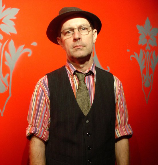 Phillip Johnston - red background, wearing a hat