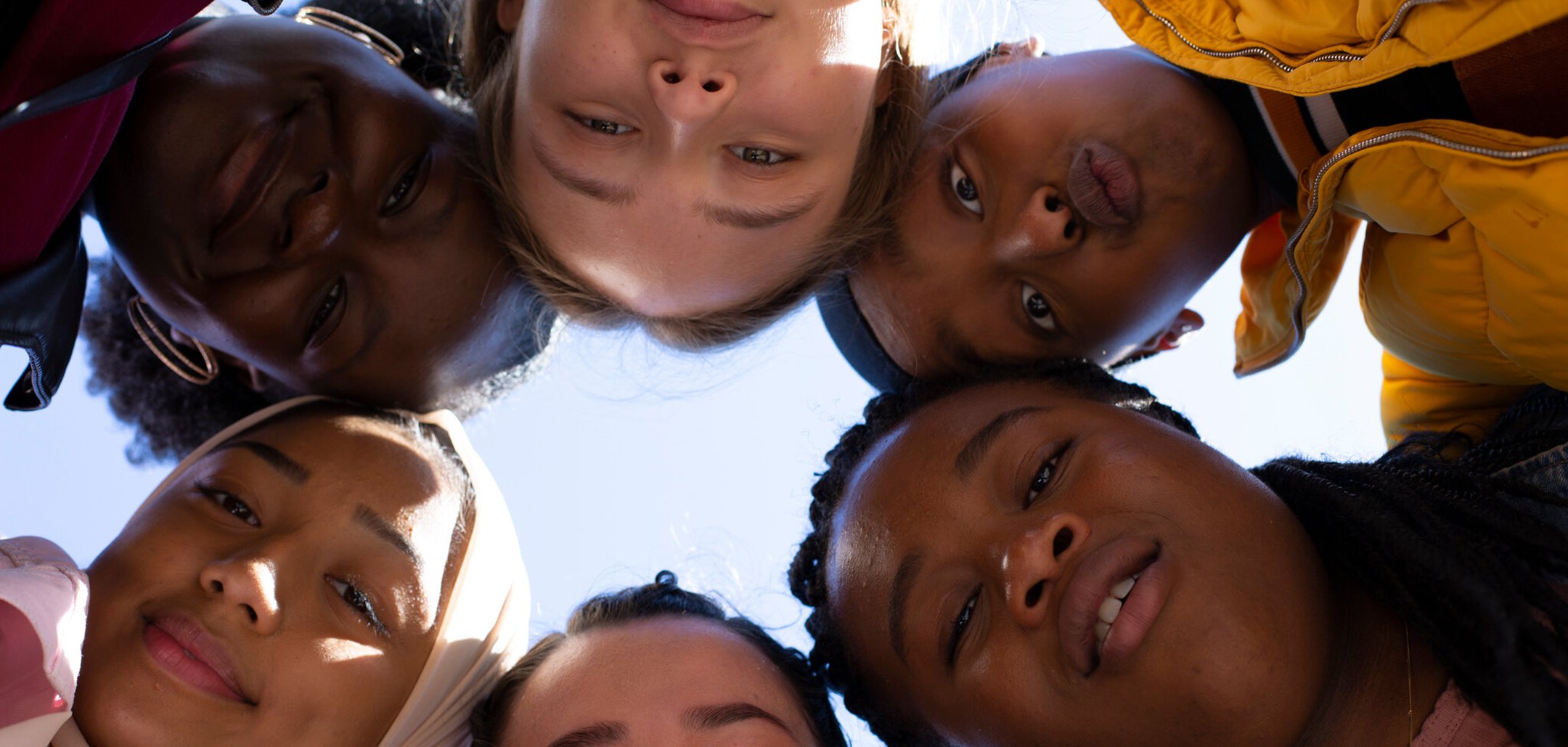 A shot from below of the young, diverse cast of the film 'Rocks' (2017) with their heads together in a circle.