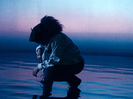 A still of a character from 'ear for eye' (2021) crouching in silhouette against a blue-purple-hued backdrop on a floor resembling water.