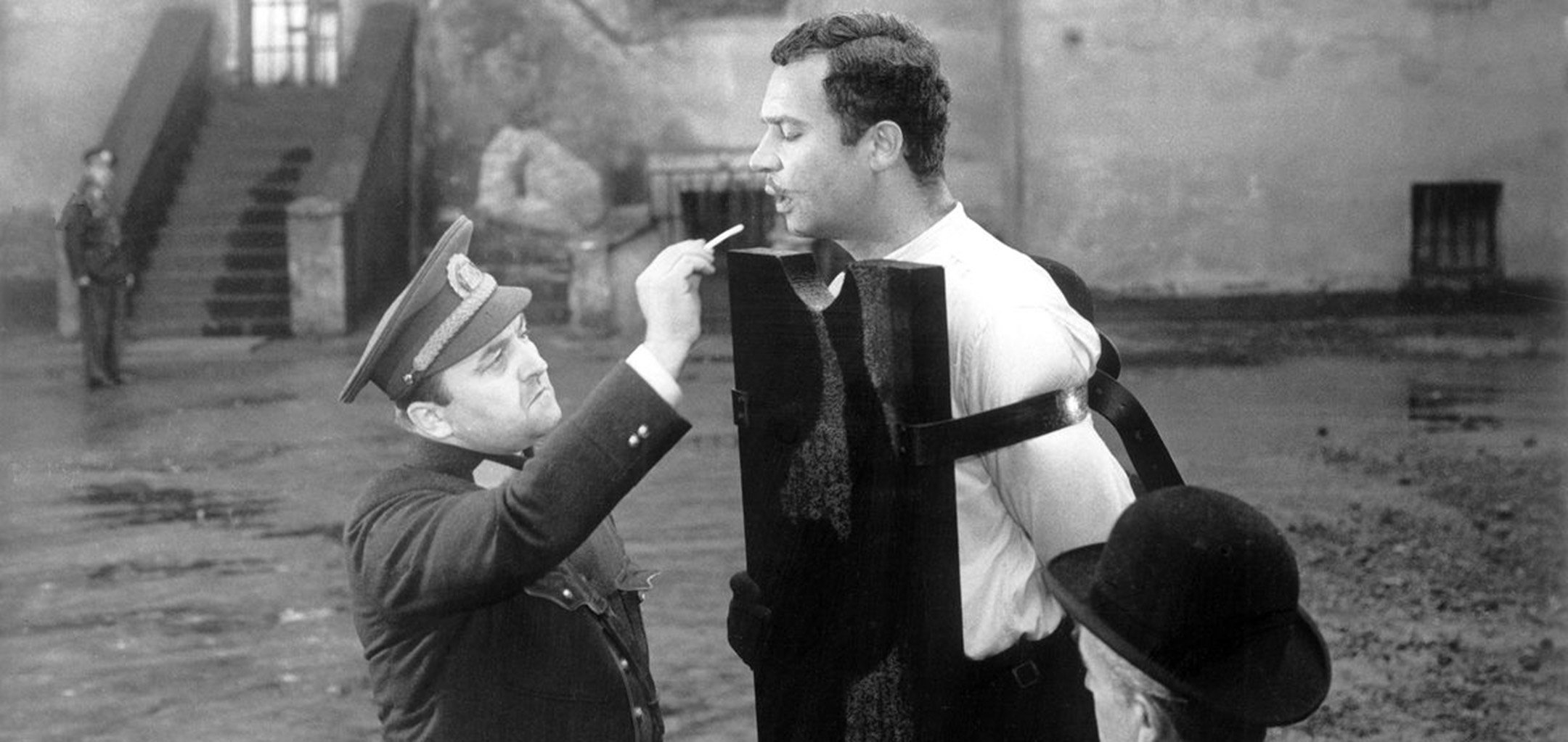 Policeman giving a man in stocks a cigarette in Happy End (1967)