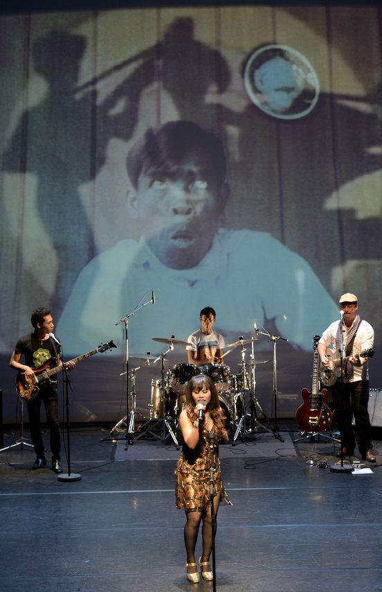 a band perform on stage with an image of a man pulling a face projected behind them