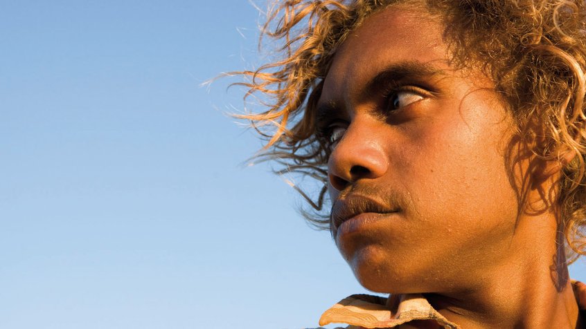 A closeup side view of Rowan McNamara's face. He has curly, tangled blonde and brown hair and he is looking to the right.